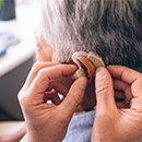 Middle section of Caucasian male doctor applying hearing aid to senior mixed race woman ear in clinic at retirement home
